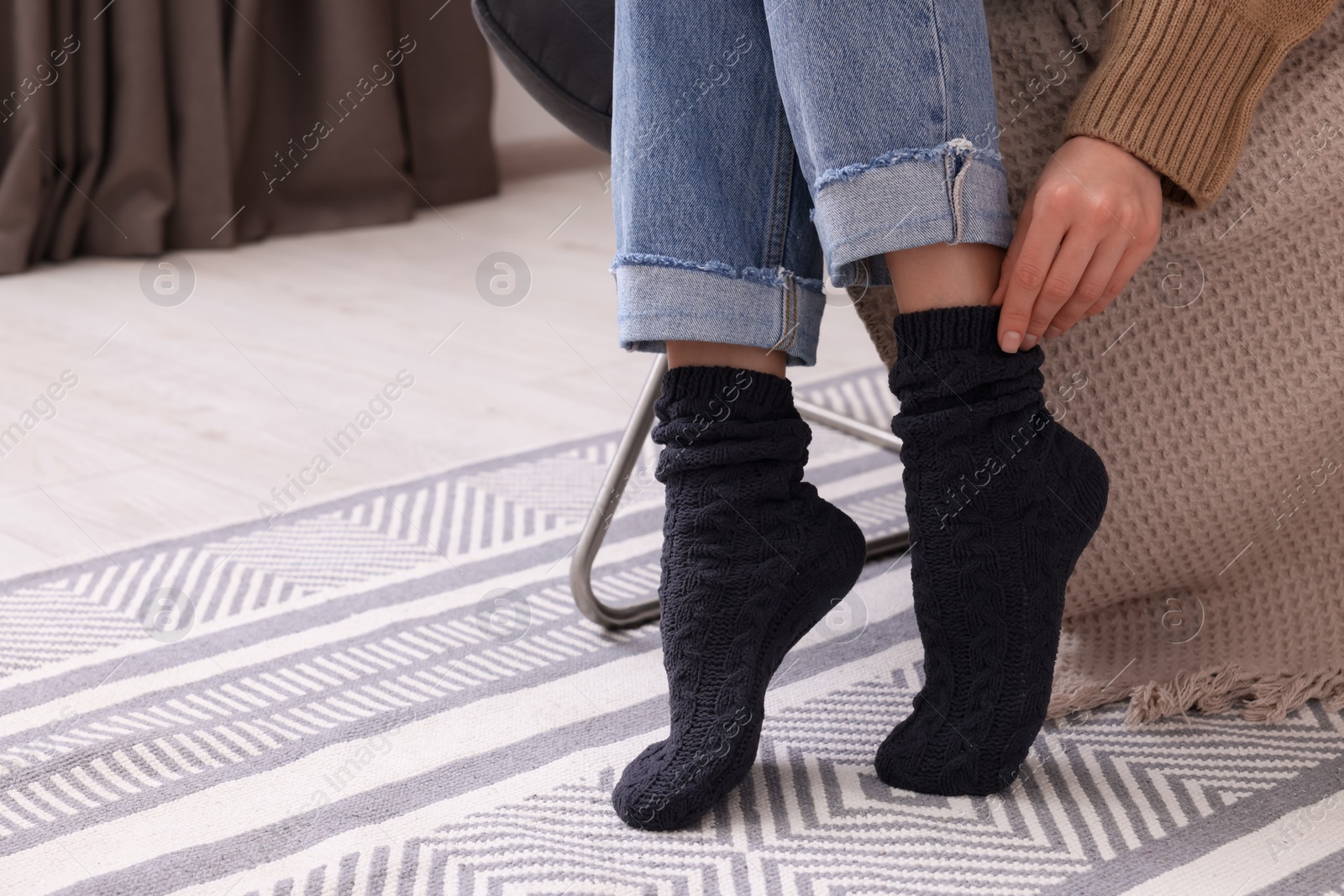 Photo of Woman wearing warm knitted socks at home, closeup