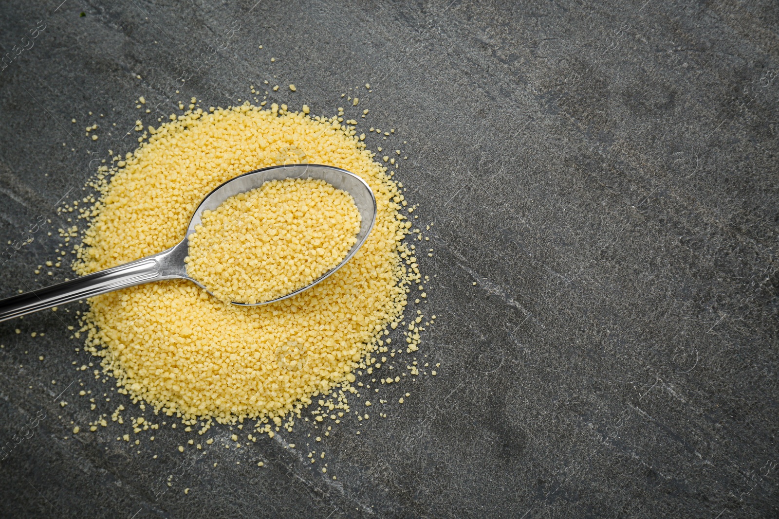 Photo of Spoon with raw couscous on grey table, top view. Space for text