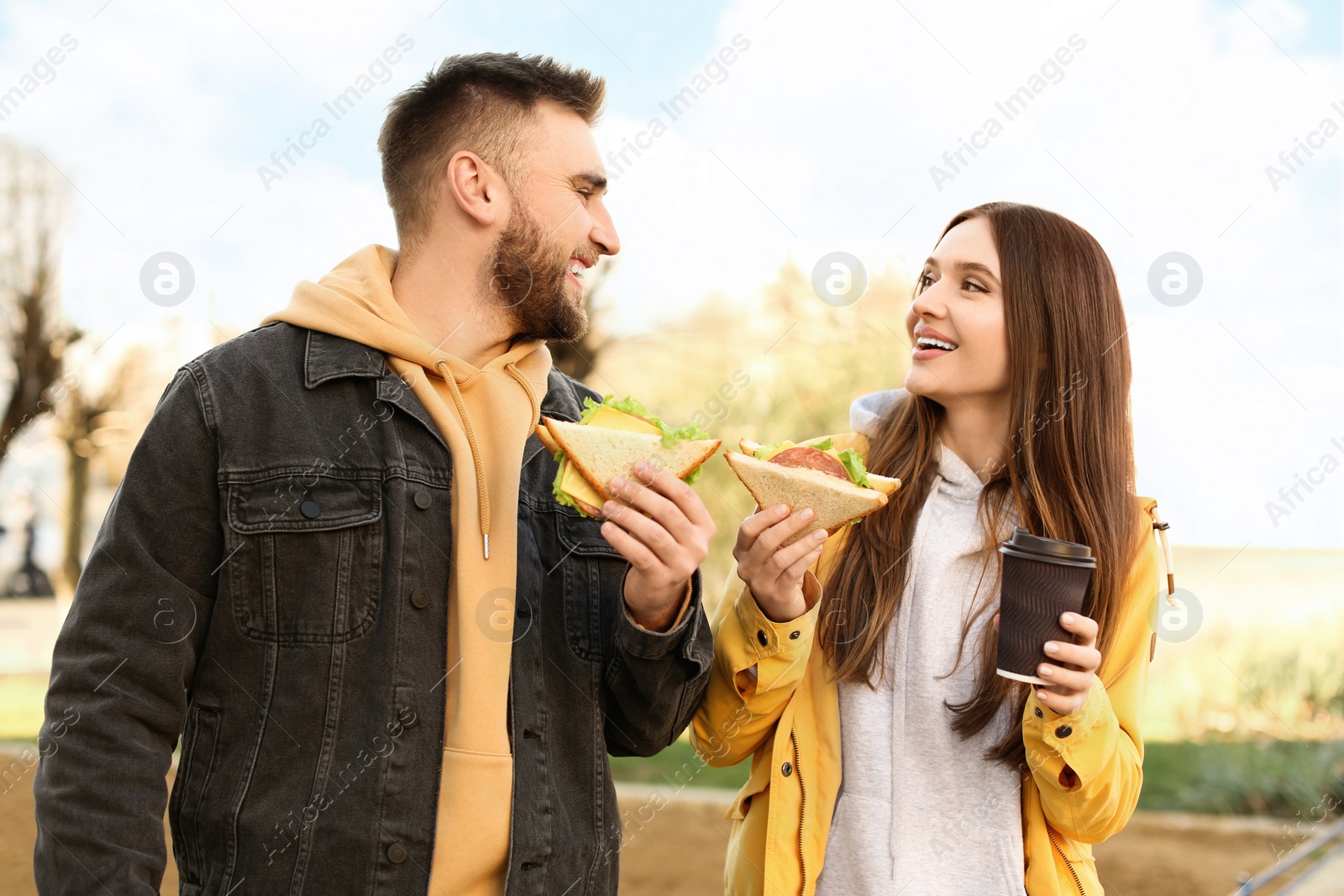 Photo of Happy young couple with sandwiches and coffee on city street