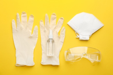Flat lay composition with medical gloves, mask and hand sanitizer on yellow background
