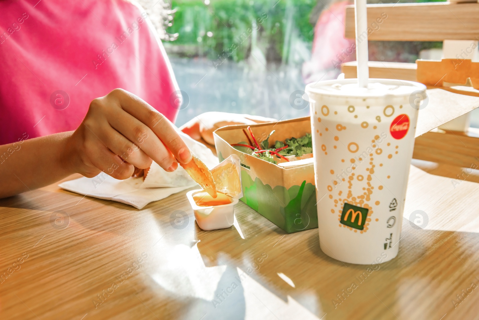 Photo of WARSAW, POLAND - SEPTEMBER 16, 2022: Woman eating fried potato at table in McDonald's cafe, closeup