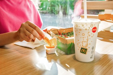 WARSAW, POLAND - SEPTEMBER 16, 2022: Woman eating fried potato at table in McDonald's cafe, closeup