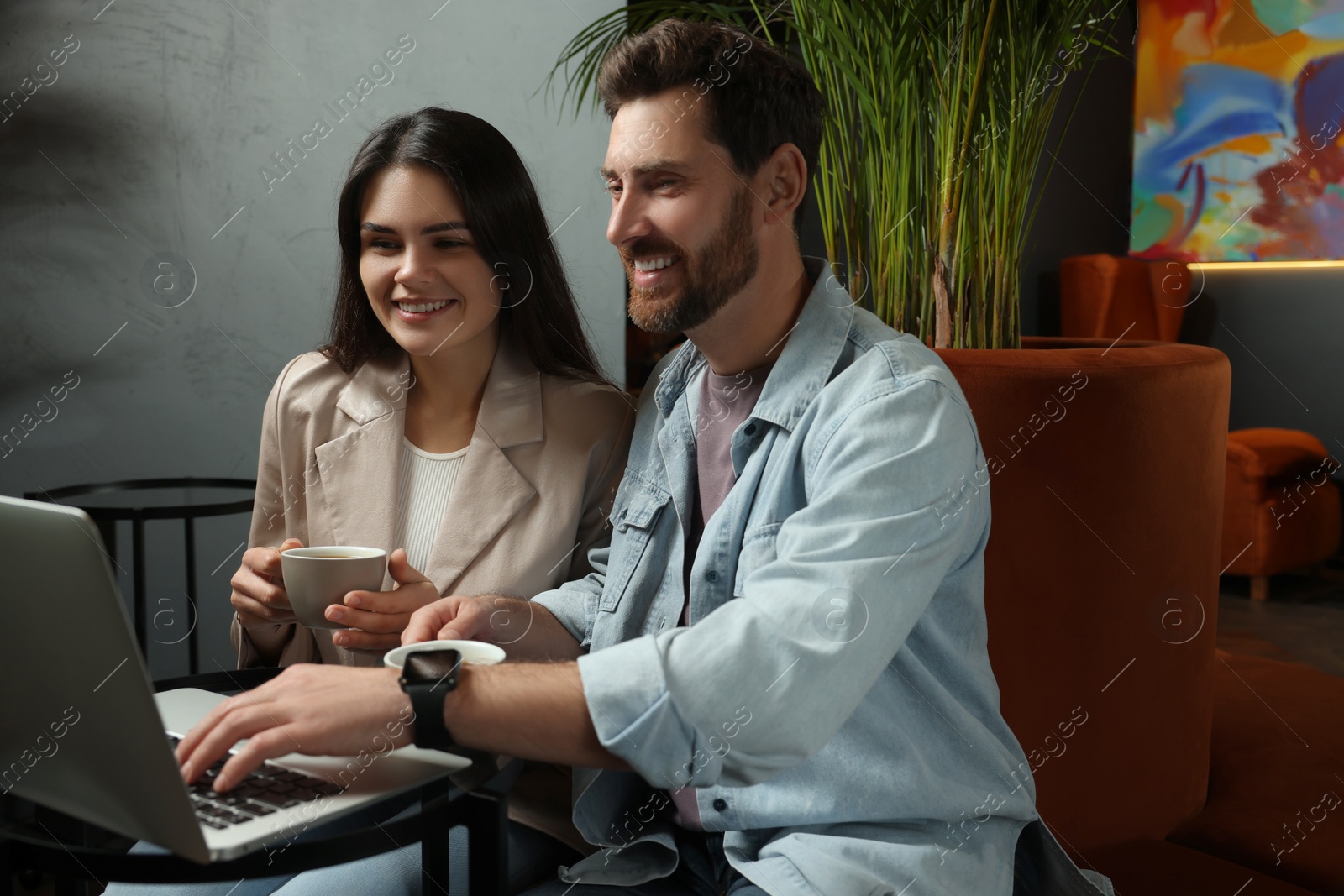 Photo of Couple with coffee and laptop spending time together in cafe