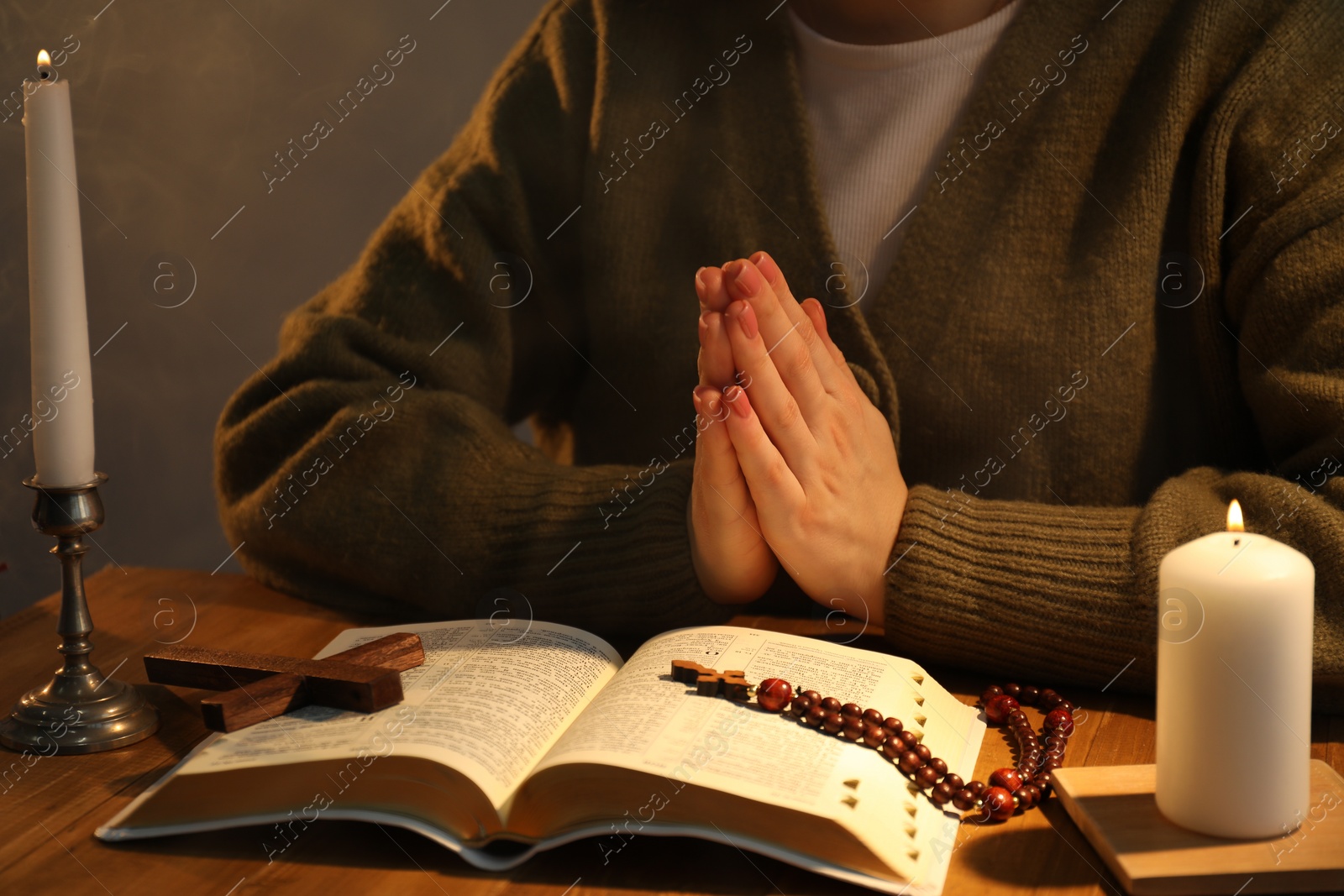 Photo of Woman praying at table with burning candles and Bible, closeup