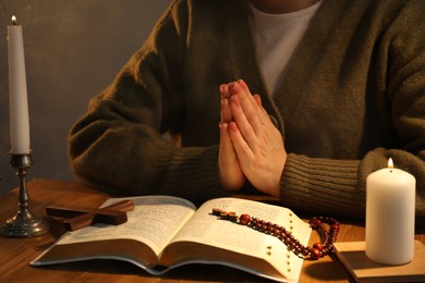 Woman praying at table with burning candles and Bible, closeup