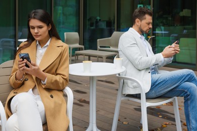 Photo of Upset arguing couple with smartphones in outdoor cafe. Relationship problems