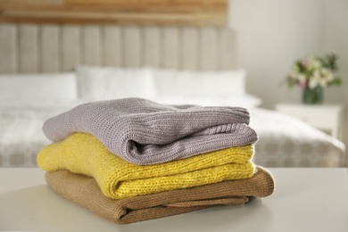 Stack of knitted sweaters on white table indoors