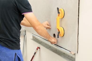 Photo of Worker using suction plate for tile installation indoors, closeup