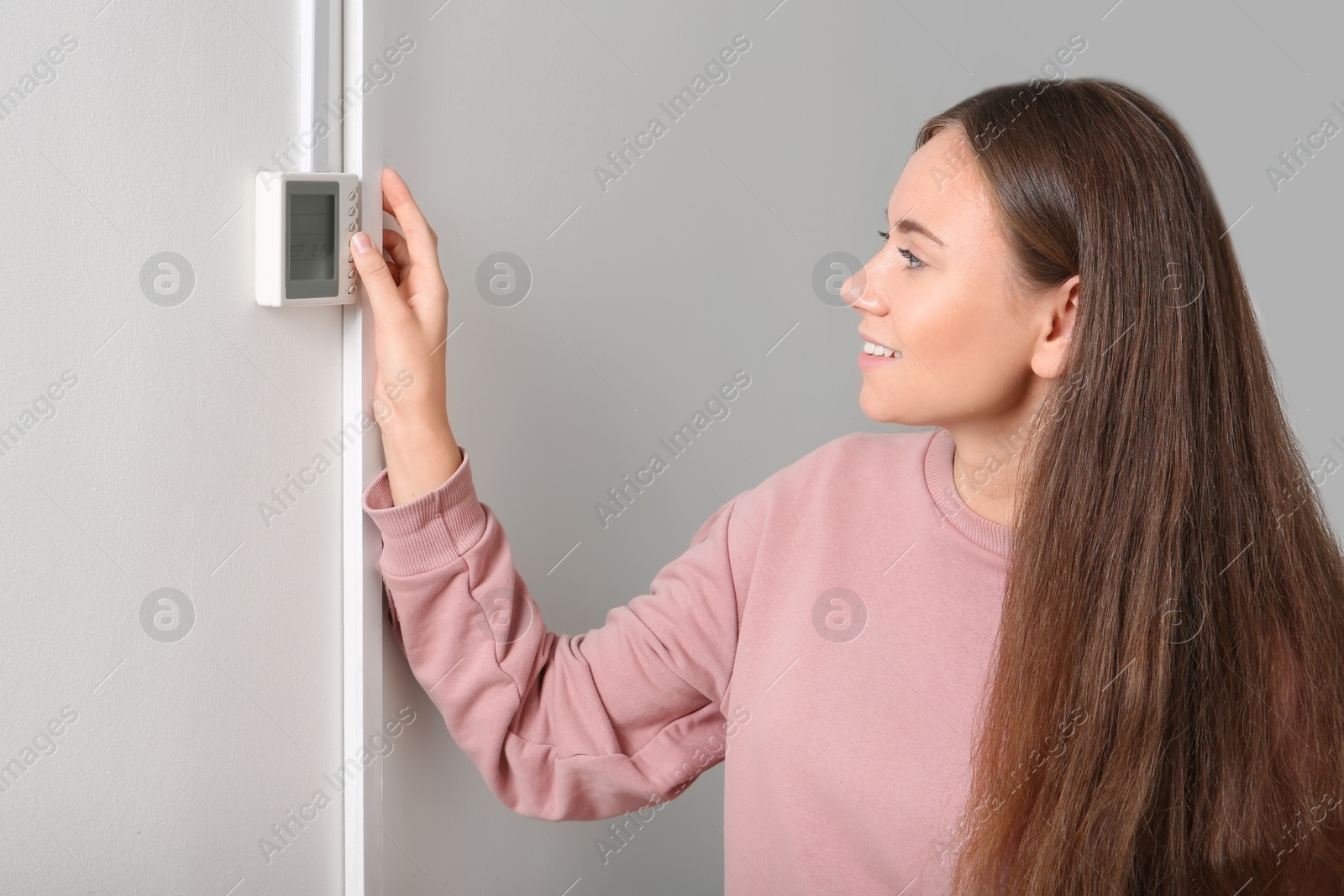 Photo of Woman adjusting thermostat on white wall. Heating system