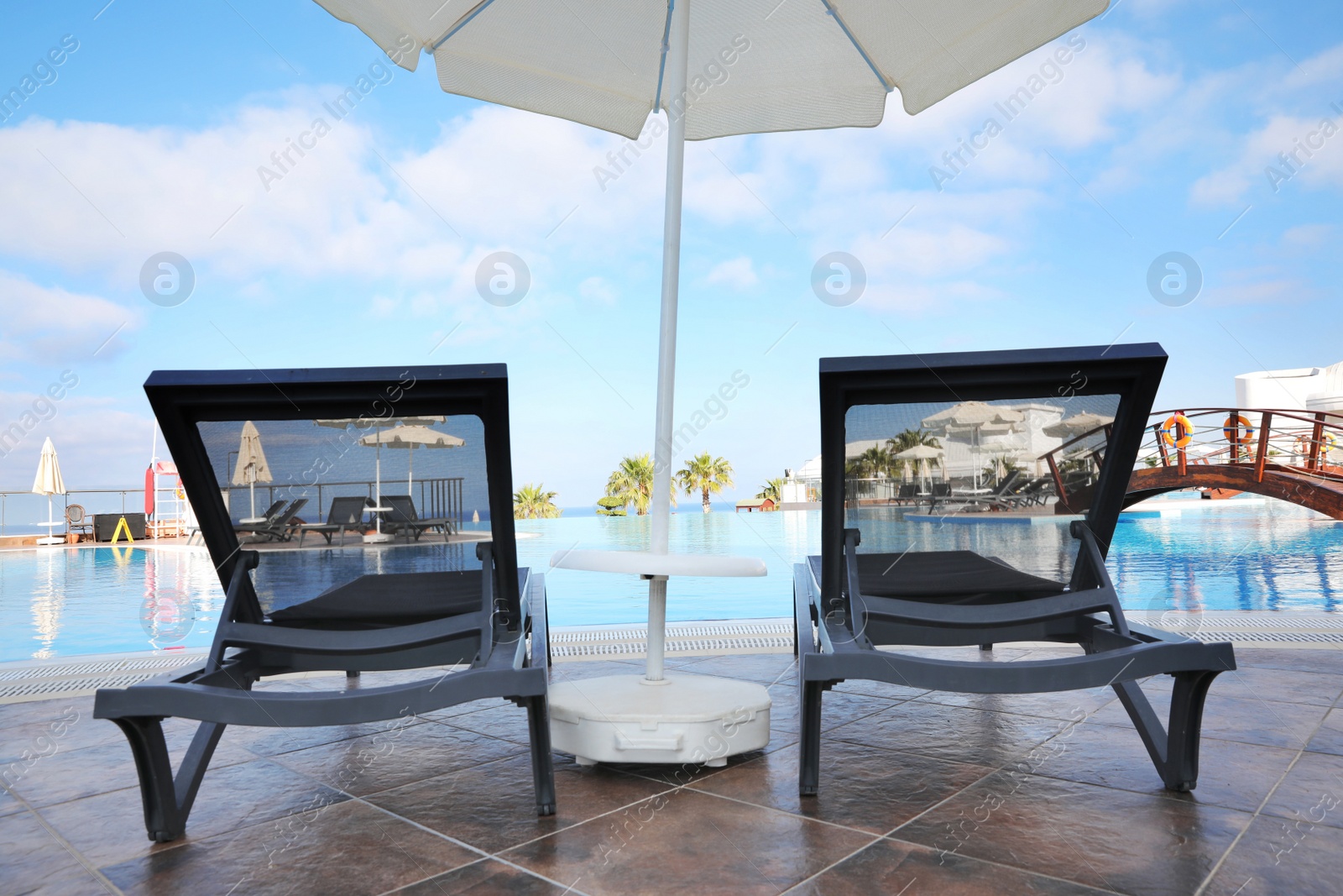 Photo of Chaise longues and beach parasol near outdoor swimming pool at resort