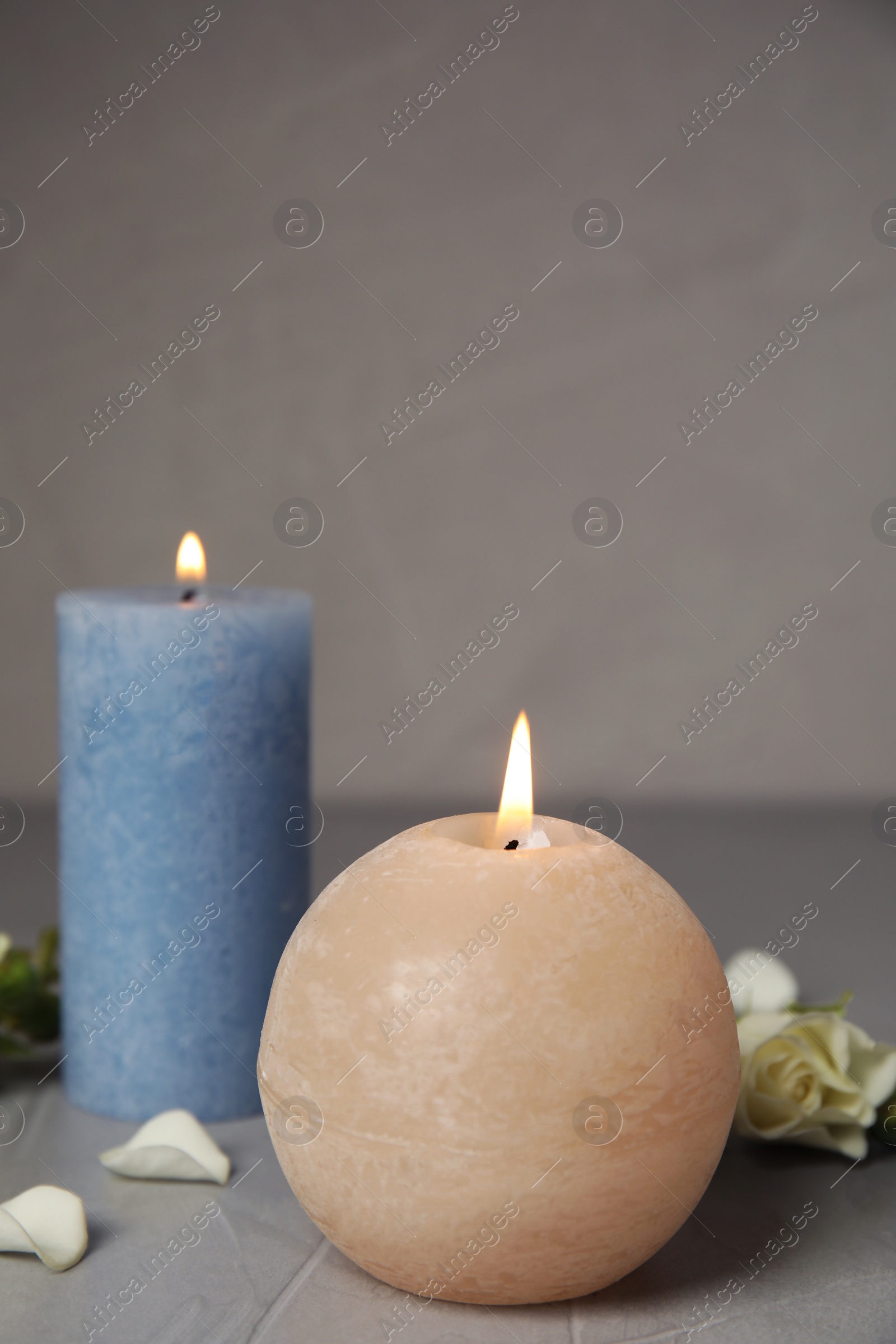 Photo of Burning candles and flowers on grey table, space for text