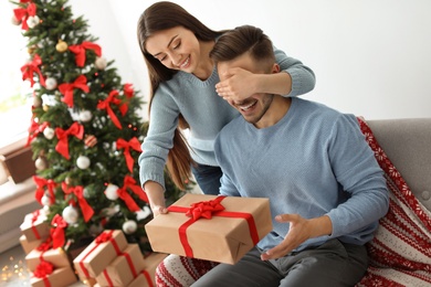 Young woman surprising her boyfriend with Christmas gift at home