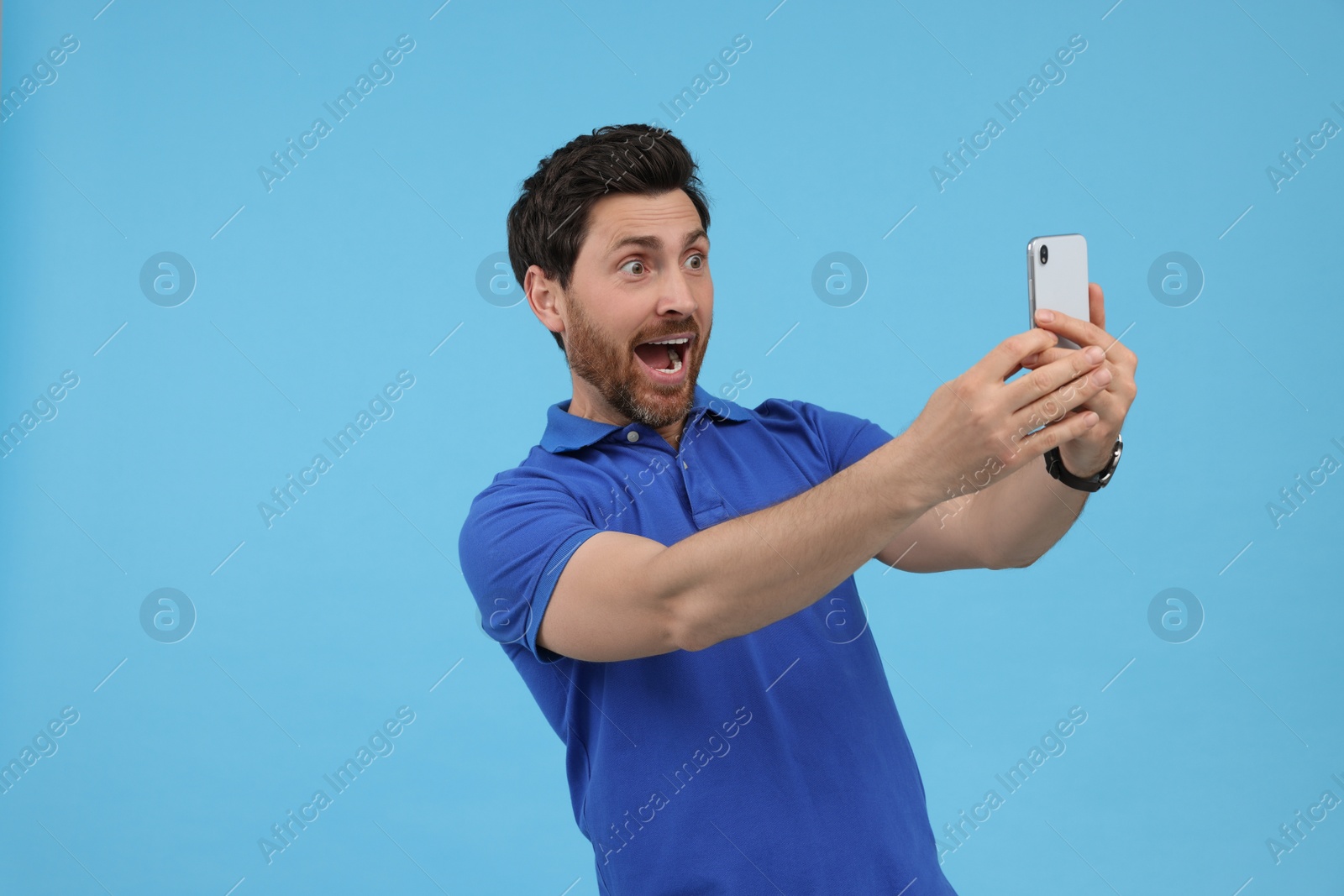 Photo of Surprised man taking selfie with smartphone on light blue background