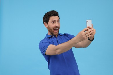 Surprised man taking selfie with smartphone on light blue background