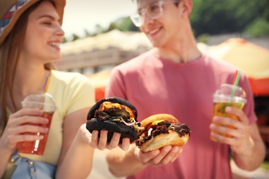 Photo of Young happy couple with burgers walking on city street, closeup