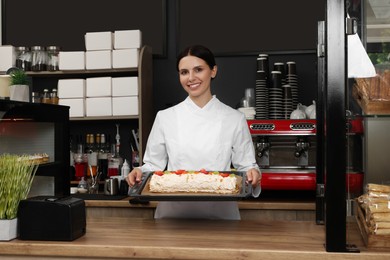 Photo of Happy baker presenting delicious cake with strawberries in cafe