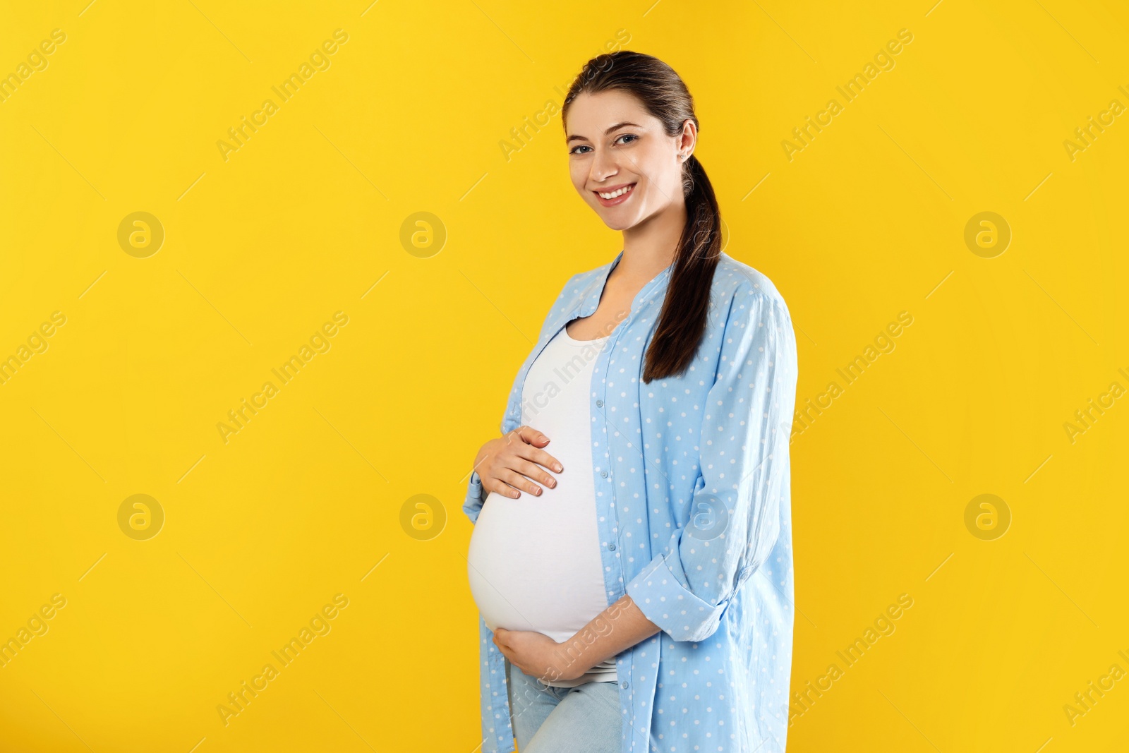 Photo of Happy young pregnant woman on yellow background, space for text