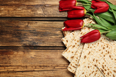 Photo of Tasty matzos and flowers on wooden table, flat lay with space for text. Passover (Pesach) Seder