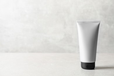 Photo of Tube of men's facial cream on light stone table. Mockup for design