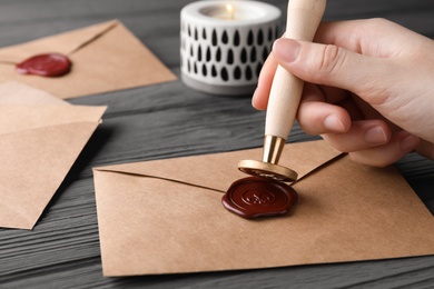 Photo of Woman sealing envelope at black wooden table, closeup