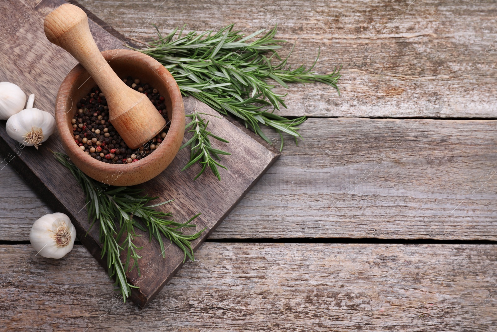 Photo of Rosemary, mortar and garlic on wooden table, flat lay. Space for text