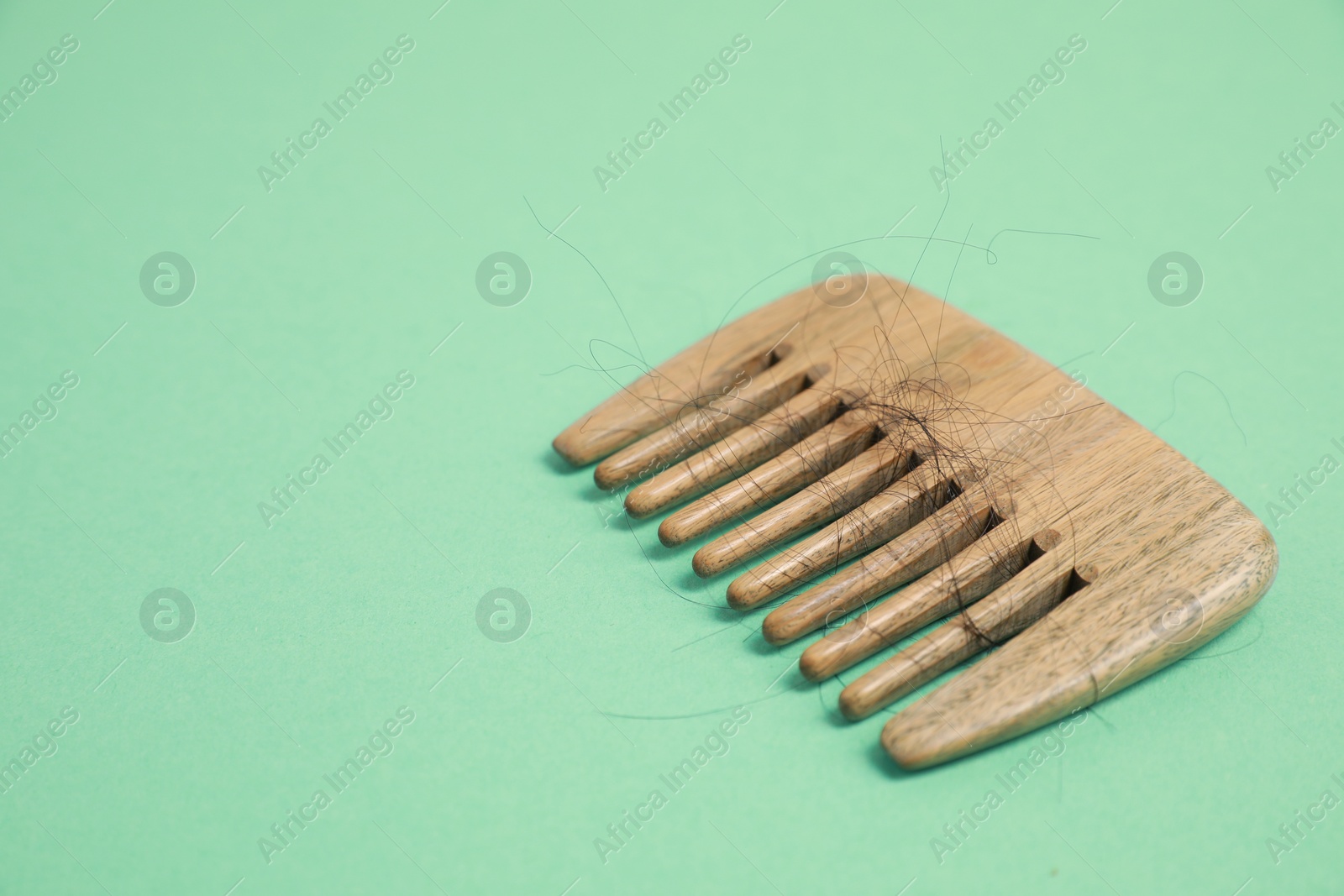 Photo of Wooden comb with lost hair on green background. Space for text