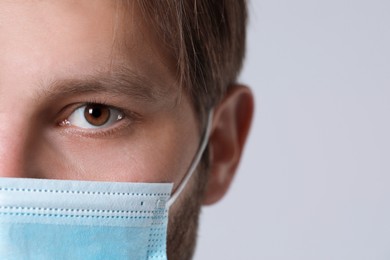Photo of Doctor or medical assistant (male nurse) with protective mask on light grey background, closeup. Space for text