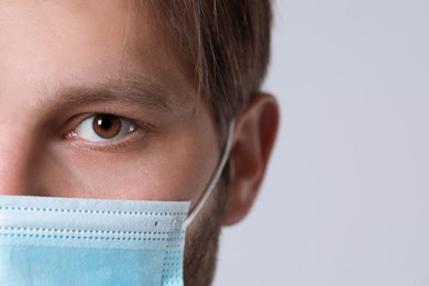 Doctor or medical assistant (male nurse) with protective mask on light grey background, closeup. Space for text