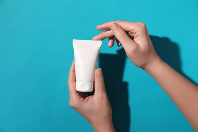 Woman with tube of hand cream on light blue background, top view