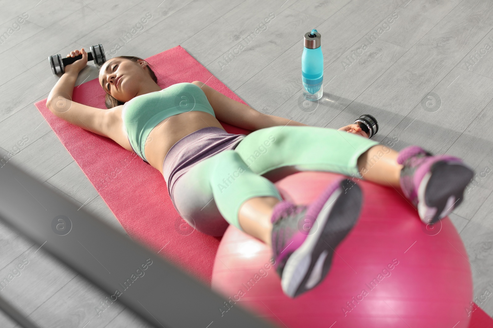 Photo of Lazy young woman with sport equipment on yoga mat indoors