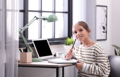 Photo of Pretty preteen girl doing homework at table in room