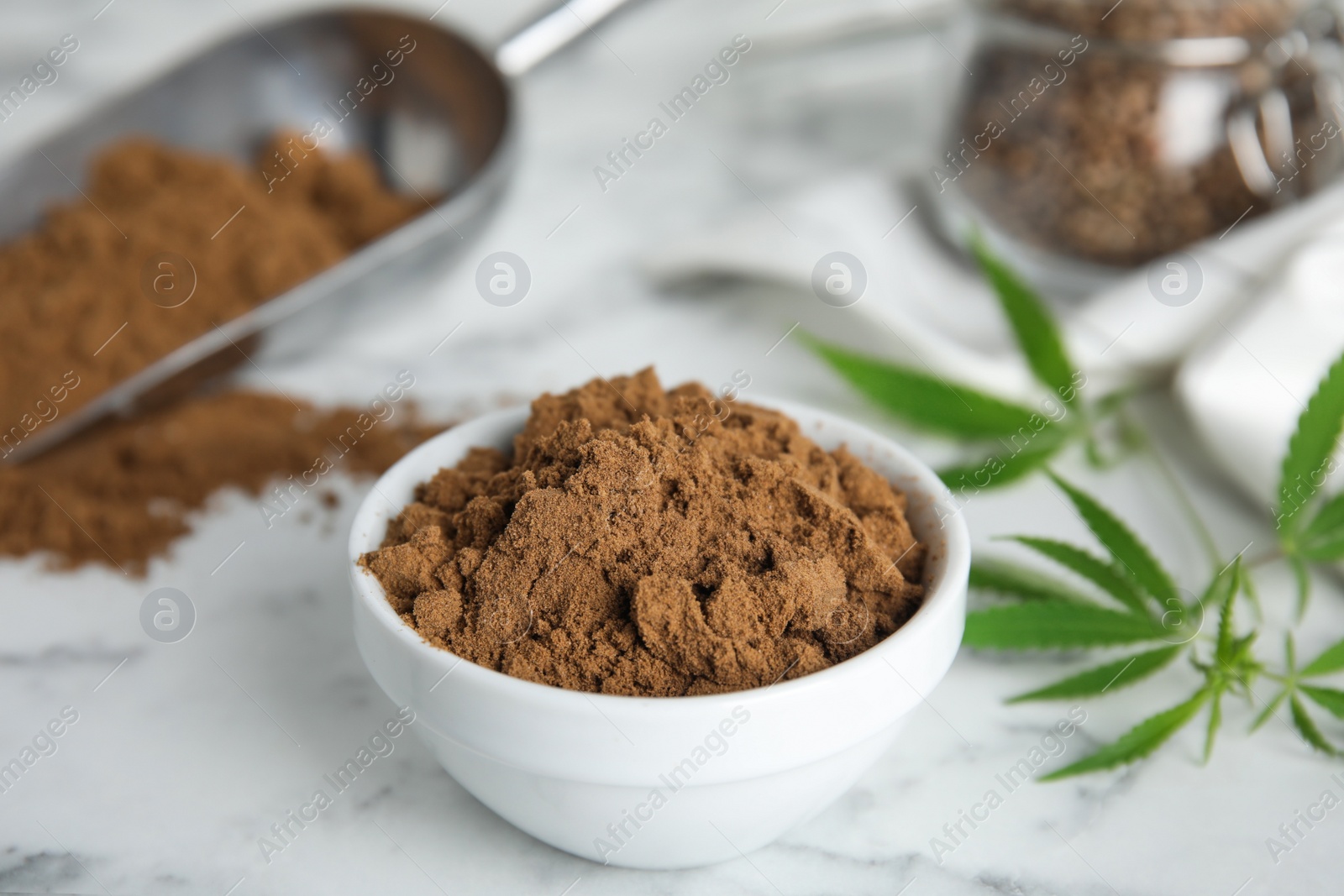 Photo of Hemp protein powder and fresh leaves on white marble table, closeup