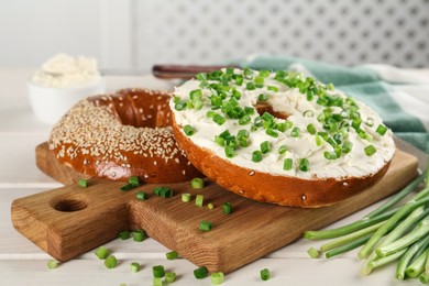 Photo of Delicious bagel with cream cheese and green onion on white wooden table