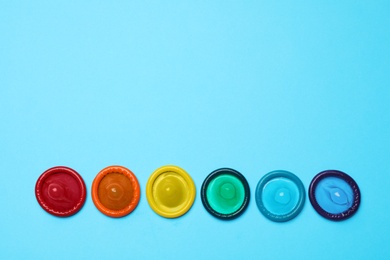 Photo of Colorful condoms on light blue background, flat lay. LGBT concept