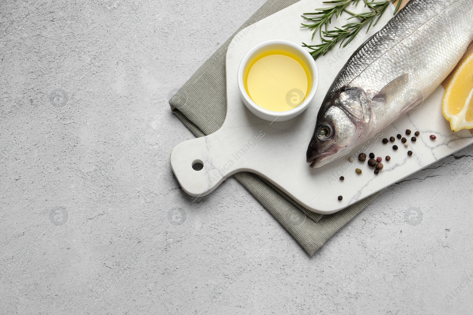 Photo of Sea bass fish and ingredients on light grey table, above view. Space for text