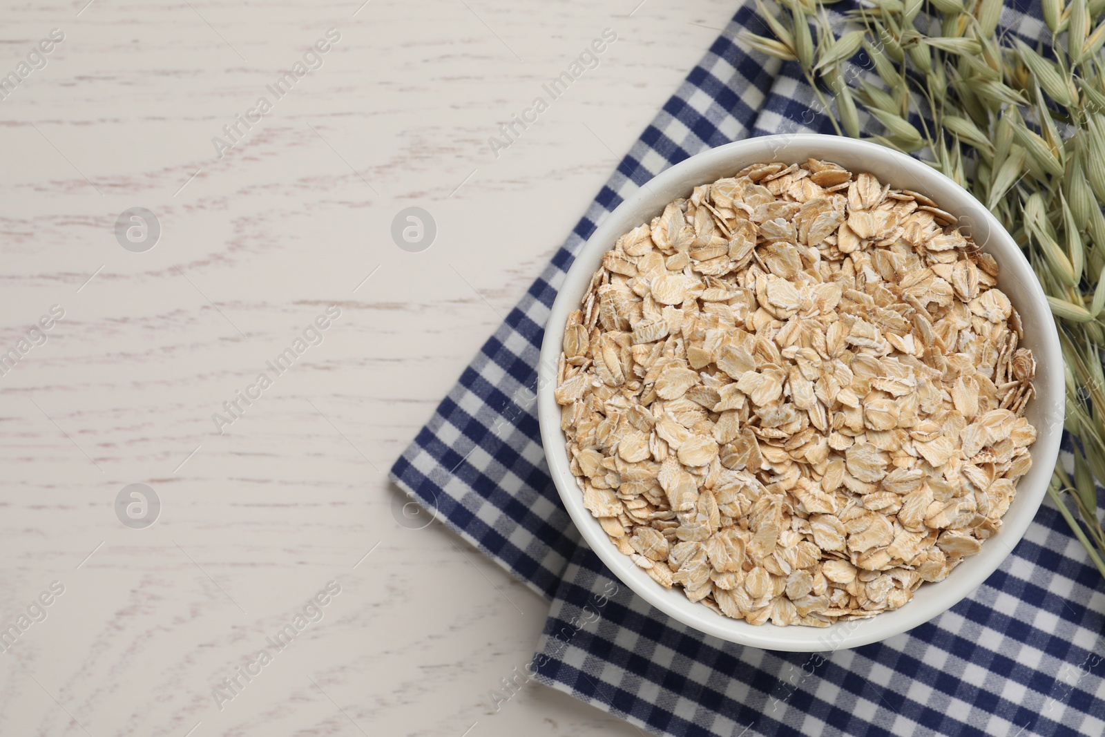 Photo of Bowl of oatmeal and branches with florets on white wooden table, top view. Space for text