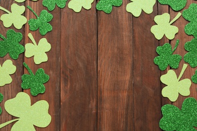 Photo of Frame made of decorative clover leaves on wooden table, flat lay with space for text. Saint Patrick's Day celebration