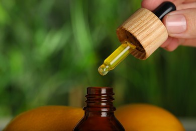 Photo of Woman dripping essential oil into bottle against blurred background, closeup