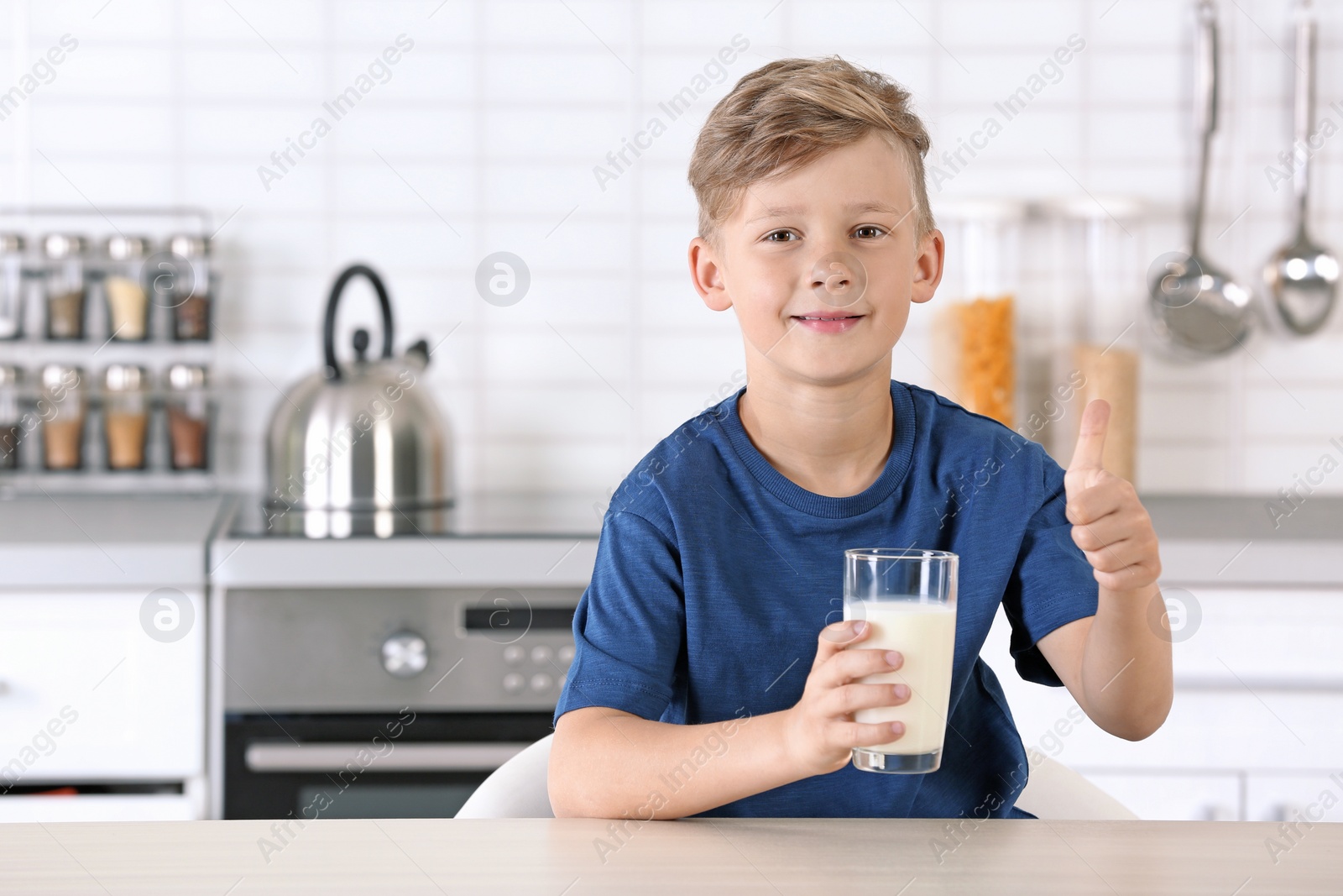 Photo of Adorable little boy with glass of milk in kitchen