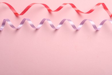 Colorful serpentine streamers on pink background, flat lay. Space for text