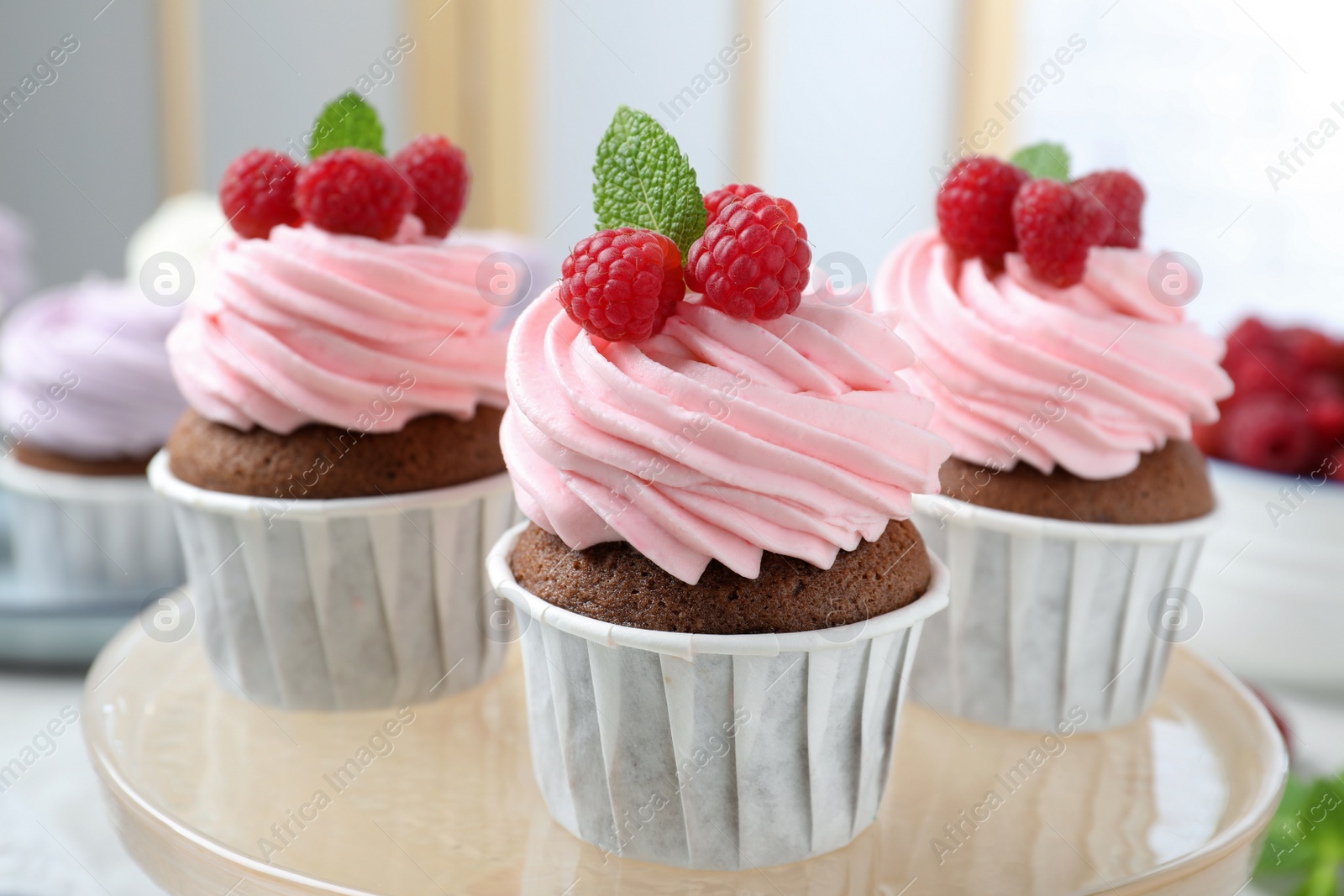 Photo of Delicious cupcakes with cream and raspberries on stand, closeup