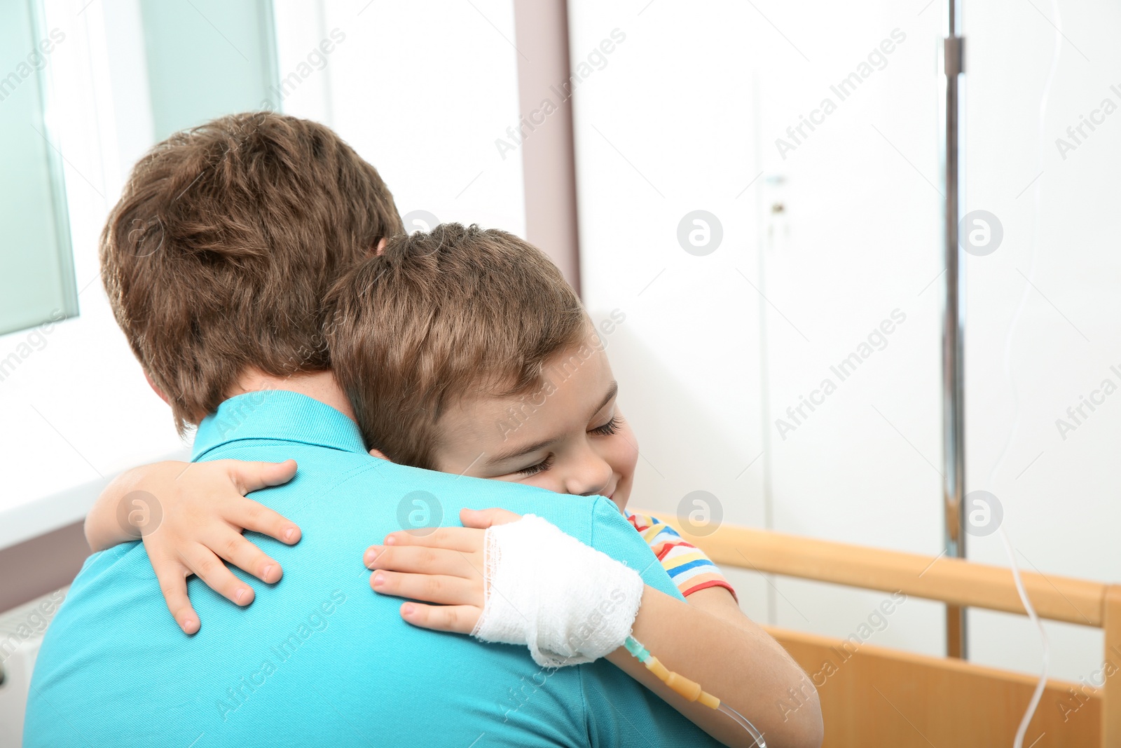 Photo of Little child with intravenous drip hugging his father in hospital
