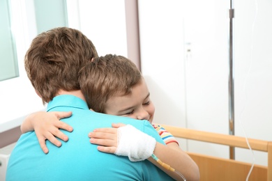 Little child with intravenous drip hugging his father in hospital