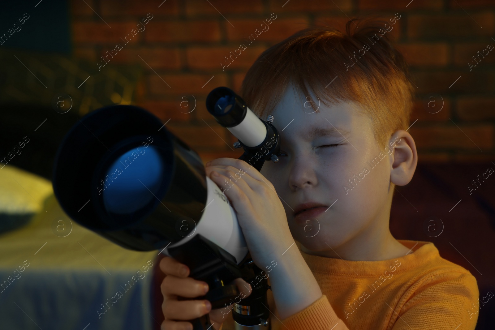 Photo of Little boy looking at stars through telescope in room