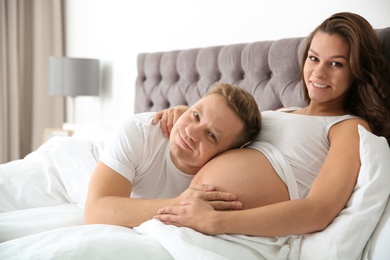 Photo of Pregnant woman with her husband in bedroom. Happy young family