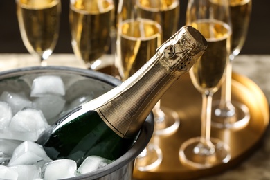 Bottle of champagne in bucket with ice cubes on table, closeup