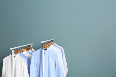 Racks with clean clothes after dry-cleaning against color background