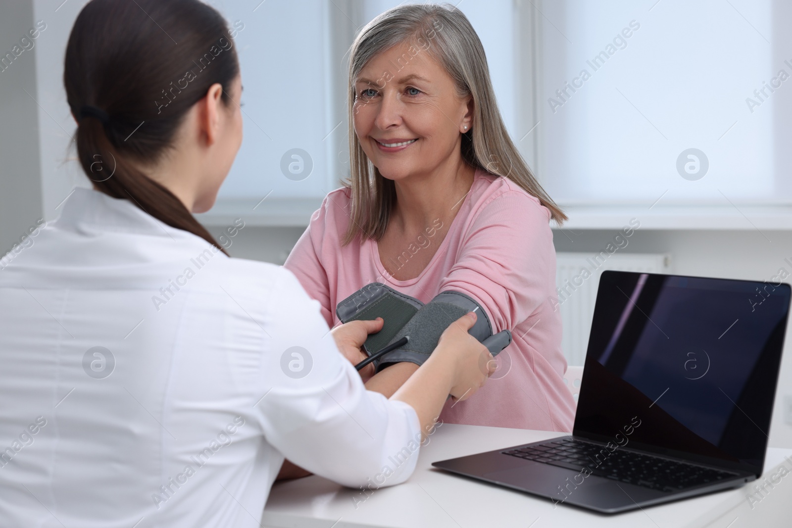 Photo of Doctor measuring blood pressure of woman at table indoors