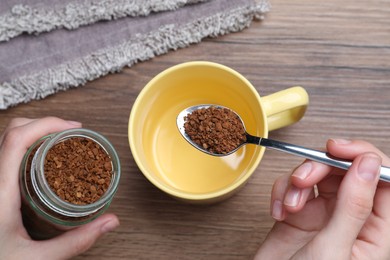 Photo of Woman pouring instant coffee into cup at wooden table, top view