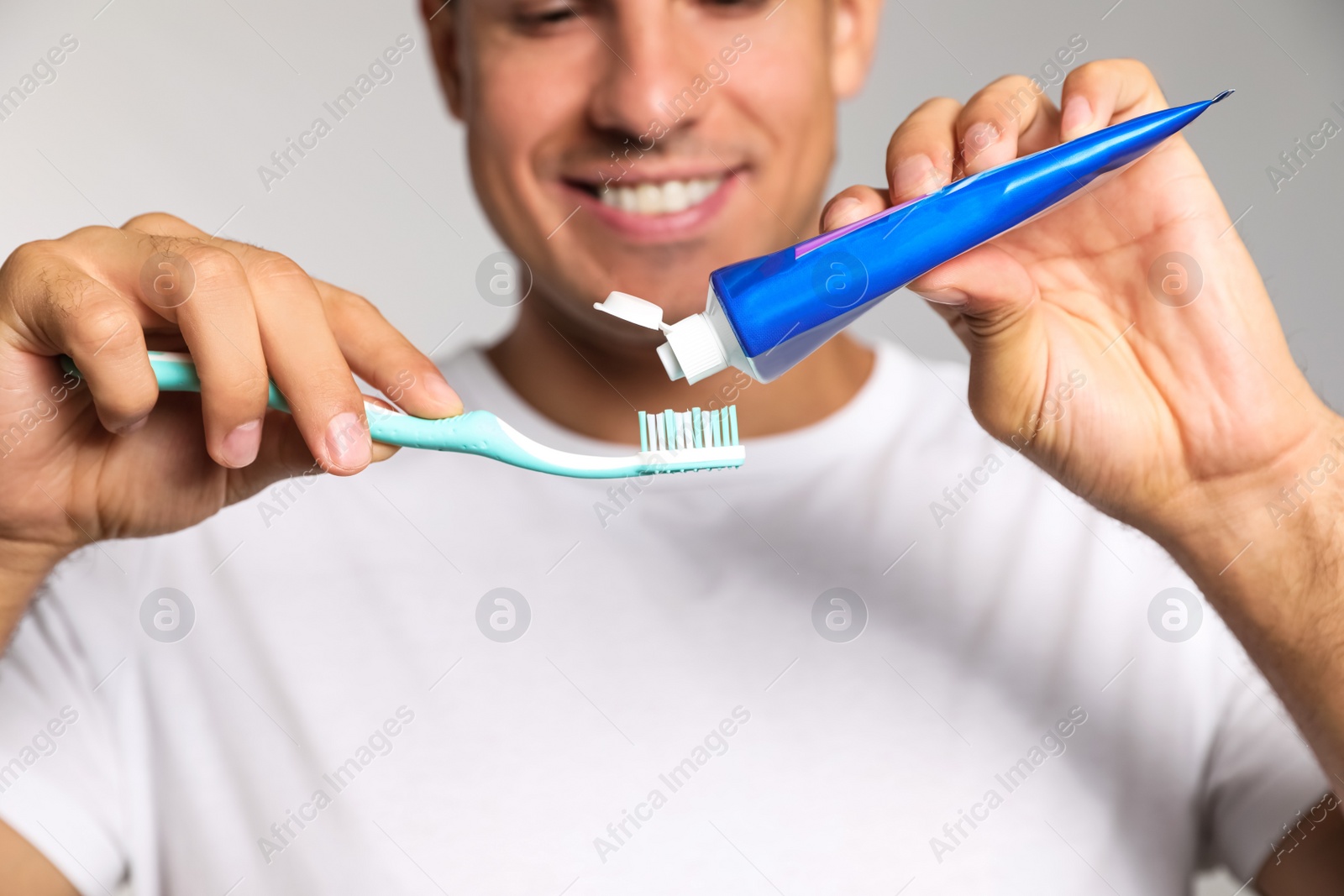 Photo of Man applying toothpaste on brush against light background, closeup